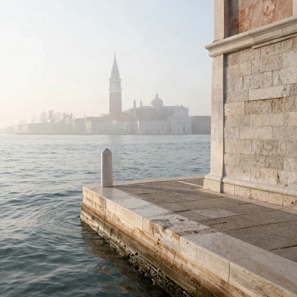 Banchina in pietra di Venezia all’alba, acqua lagunare argentea e campanile tra la foschia.